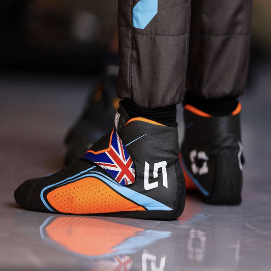 Black and orange Lando Norris 2022 F1 race shoes with British flag design on a reflective surface.