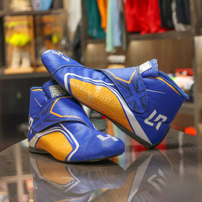 Blue and orange Lando Norris 2021 F1 Racing boots with 'LR' branding on a reflective surface.