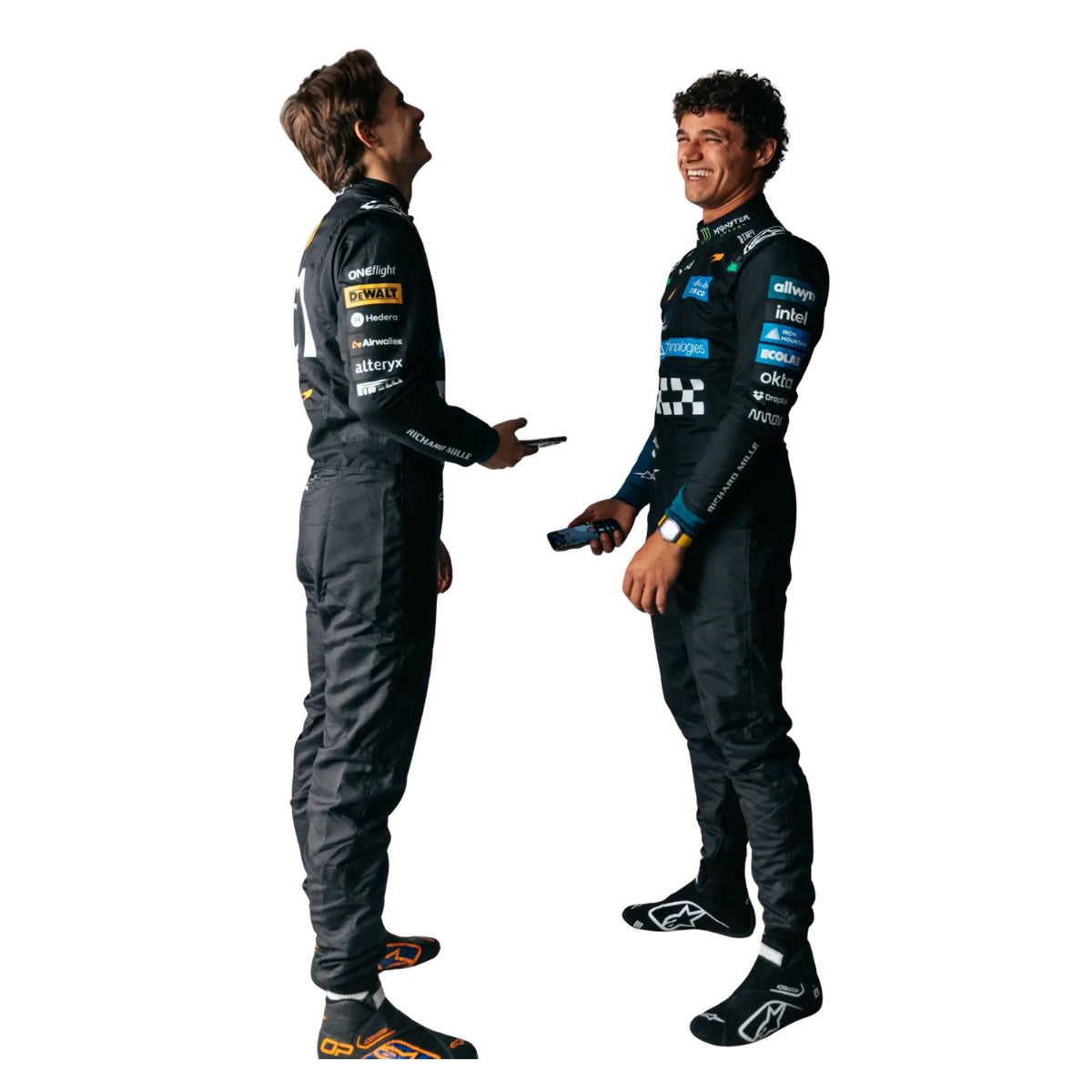 Lando Norris & Oscar Piastri in black Mclaren racing suits and Alpinestars gear standing and talking against a solid white background.