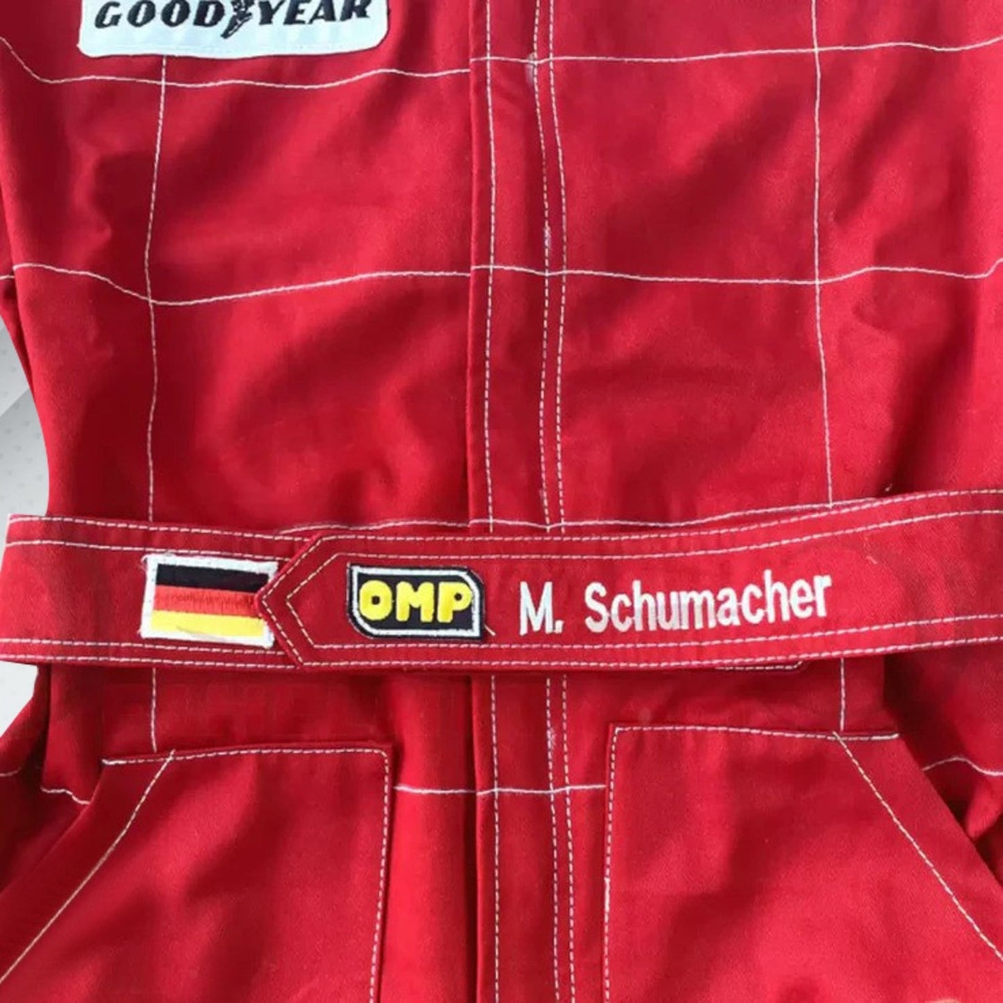 Close-up of Schumacher’s 1996 F1 suit, featuring the detailed stitching, Ferrari red color, and early sponsor branding from his debut season