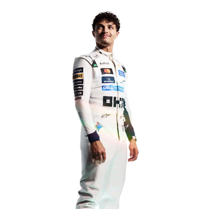 Lando Norris wearing a white and light blue racing suit with multiple sponsor logos stands with arms crossed against a plain white background.